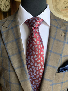 A mannequin wearing a brown suit with a red silk tie with silver floral detail.